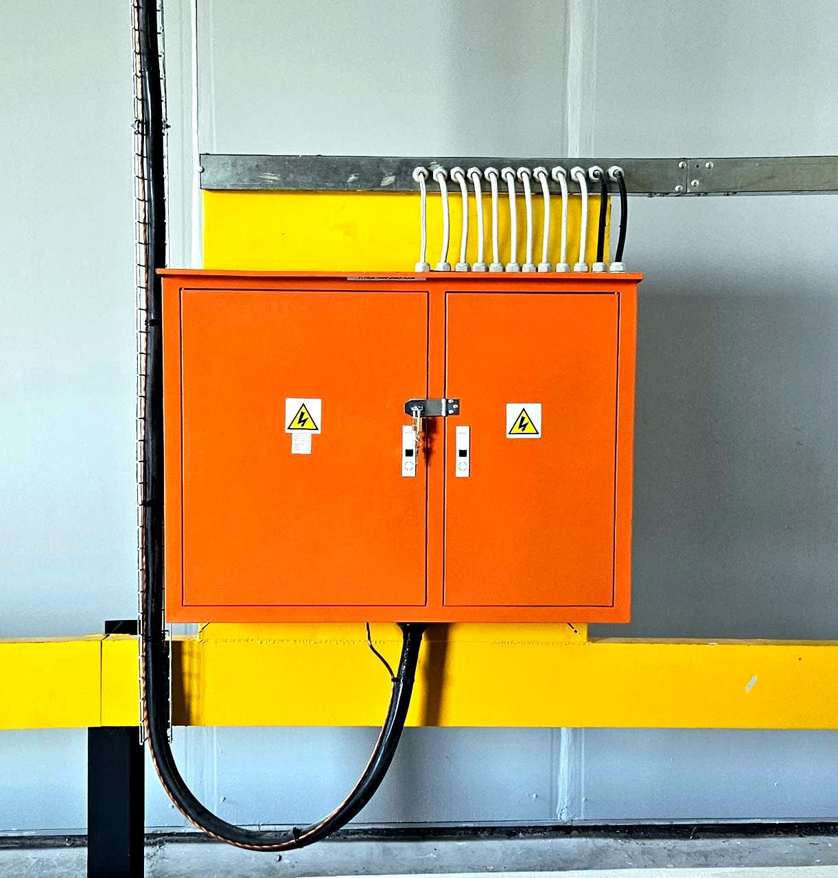 Wall-mounted electrical distribution board with cable glands and hazard warning labels.